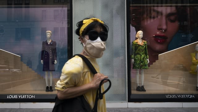 A woman wearing a mask walks by a Louis Vuitton shop in New York’s Fifth Avenue shopping district