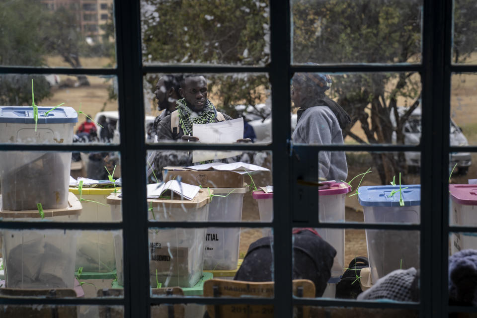 An electoral worker stands with ballot boxes lined up and ready to be stored at a collection and tallying center in Nairobi, Kenya Wednesday, Aug. 10, 2022. Kenyans are waiting for the results of a close but calm presidential election in which the turnout was lower than usual. (AP Photo/Ben Curtis)