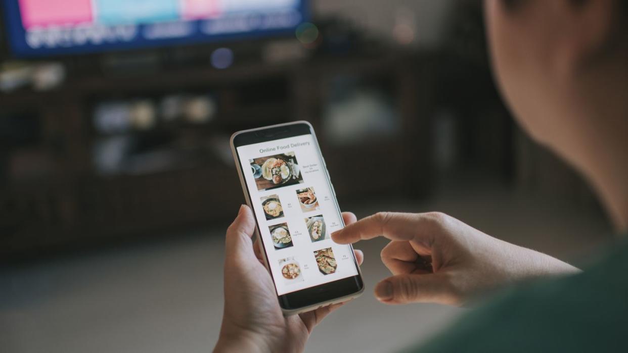 online food delivery mobile app shown on smart phone screen hold by asian woman hands in living room