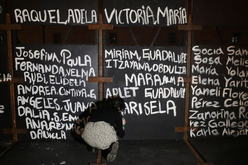 A woman paints the names of victims of femicide in Mexico on fences placed outside the National Palace ahead of a Women's Day protest, in Mexico City