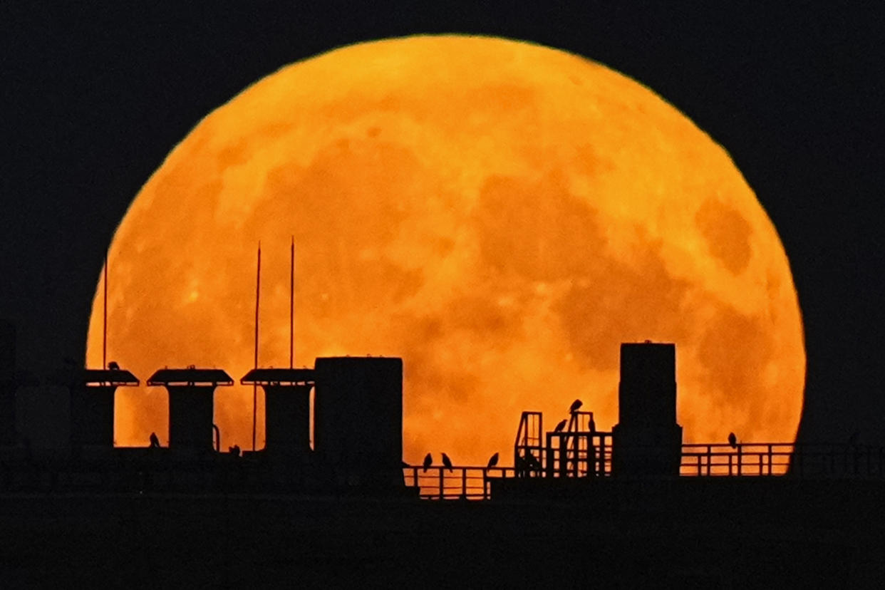 The outline of the top of a residential building is seen against the red glow of a supermoon as it rises.