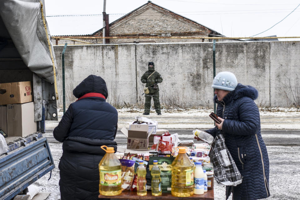 In this photo taken on Saturday, Dec. 1, 2018, A Russian border guard stands behind barbed wire on the Russian side of the Russia-Ukraine border as people buy and sell at Saturday's market in Milove, eastern Ukraine, one village, which is crossed by the main road called Friendship of People's Street and barbed wire. People on the streets easily mix both Russia and Ukrainian languages without making a political statement of it, but earlier this year, Russia built a barbed wire fence on the Friendship of People's street, marking the border with Ukraine in a metaphorical statement about the long-simmering conflict between the countries. (AP Photo/Evgeniy Maloletka)