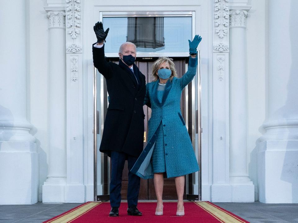 President Biden and Jill Biden wave. Jill is wearing a blue coat and dress.