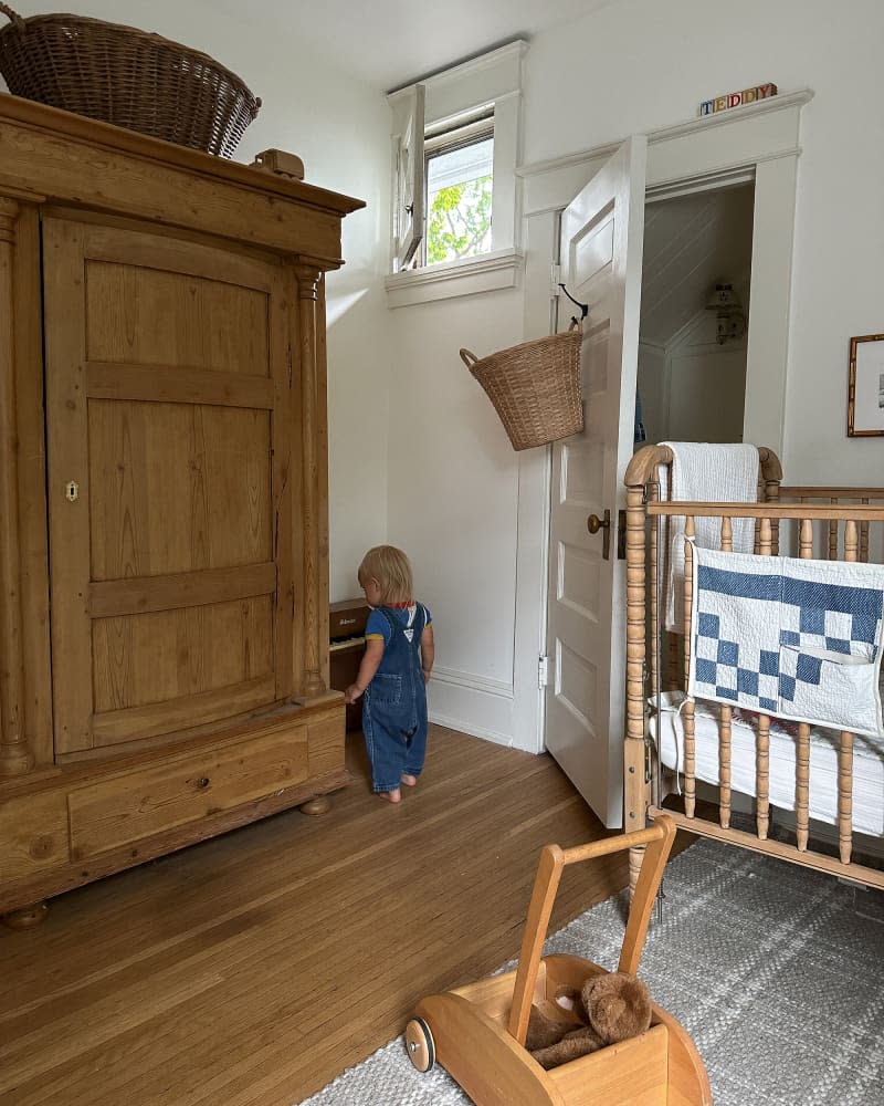 Toddler in newly renovated nursery with large wooden armoire.