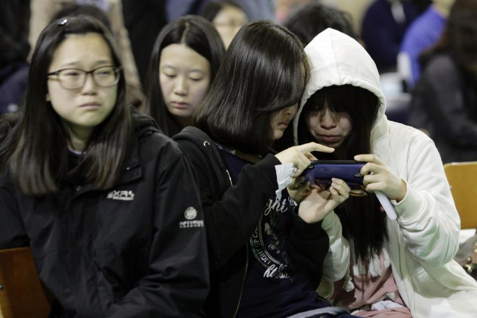 Students check their mobile phone for the latest news on the ferry that sank Wednesday, which was carrying 475 people aboard, including 325 students, at an auditorium in Danwon High School in Ansan, South Korea, Thursday, April 17, 2014. Strong currents, rain and bad visibility hampered an increasingly anxious search Thursday for 287 passengers, many thought to be high school students, still missing more than a day after their ferry flipped onto its side and sank in cold waters off the southern coast of South Korea. (AP Photo/Woohae Cho)