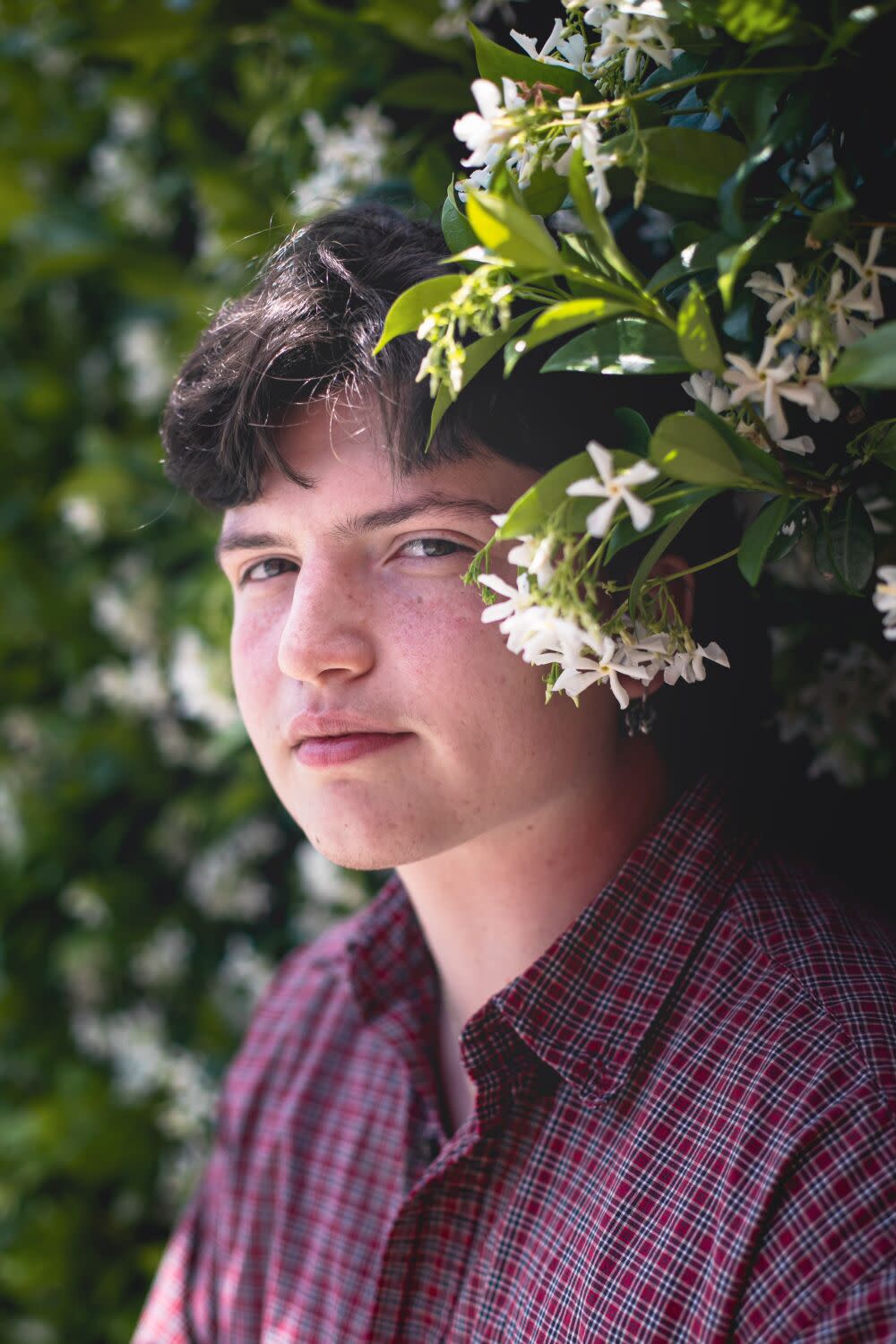 A person stands outdoors, a branch of flowering jasmine next to their head.