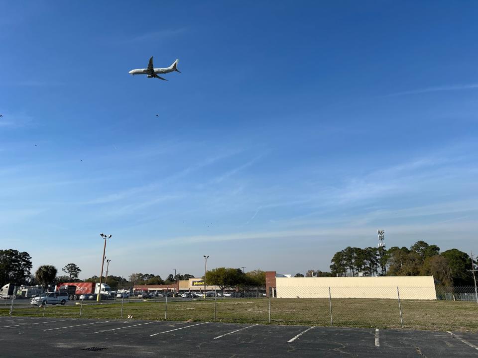 A US Navy airplane flies over the future site of a new Live Oak Public Libraries branch. The fenced-in site is located within the Eisenhower Square shopping plaza near the intersection of Eisenhower Drive and Waters Avenue.