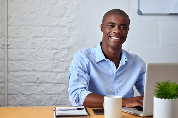 Smiling man in dress shirt, typing on laptop