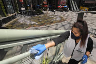Andrea Castaneda cleans the railings at Universal CityWalk, Thursday, June 11, 2020, near Universal City, Calif. The tourist attraction, which had been closed due to the coronavirus outbreak recently re-opened. The Universal Studios tour is still closed. (AP Photo/Mark J. Terrill)