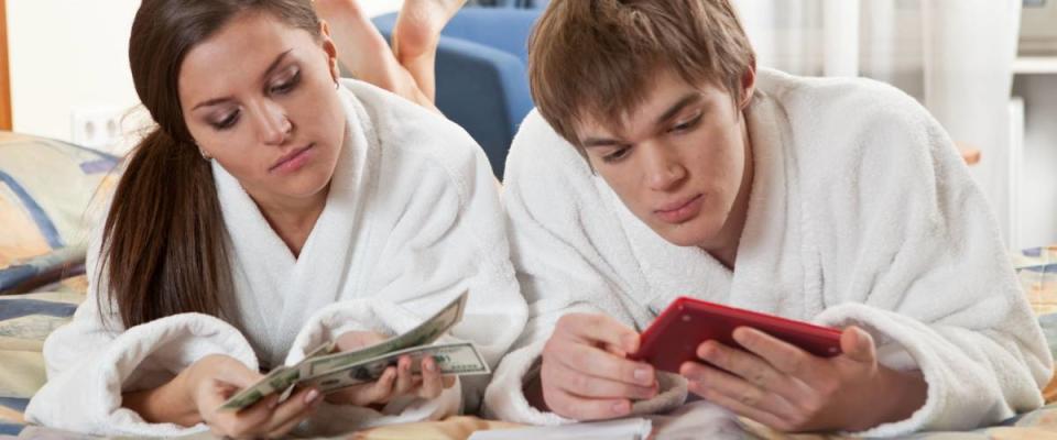 The young couple lying on the bed at home plans the family budget.
