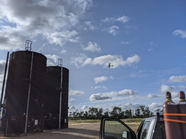 Methane is a potent greenhouse gas that's leaking from oil and gas operations, but research suggests official estimates fail to capture just how much. Here, a plane with new laser technology to measure methane emissions flies over a storage tank at an oil and gas site in B.C., trying to get more accurate data. (Submitted by Matthew Johnson - image credit)