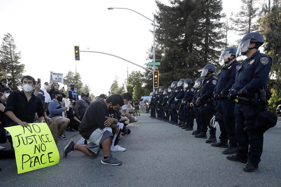 People kneel in front of a line of California Highway Patrol officers in Redwood City, Calif., Tuesday, June 2, 2020.