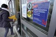 A passer-by enters a pharmacy with a vaccination advisory attached to a door, right, Thursday, Dec. 2, 2021, in Worcester, Mass. As the U.S. recorded its first confirmed case of the omicron variant, doctors across the country are experiencing a more imminent crisis with a delta variant that is sending record numbers of people to the hospital in New England and the Midwest. (AP Photo/Steven Senne)