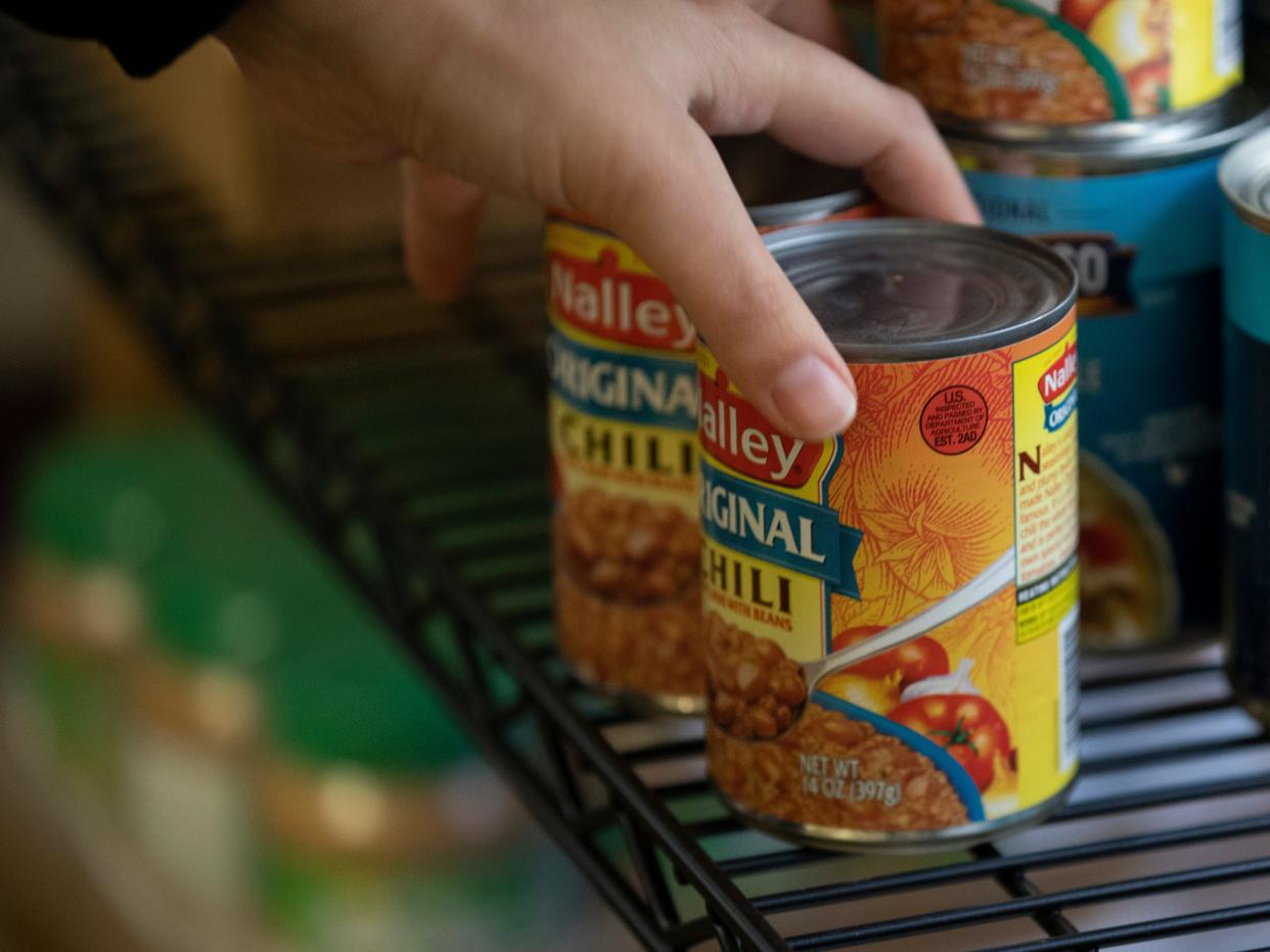 A Marion Polk Food Share employee arranges cans on a shelf at Aware Food Bank in Woodburn.