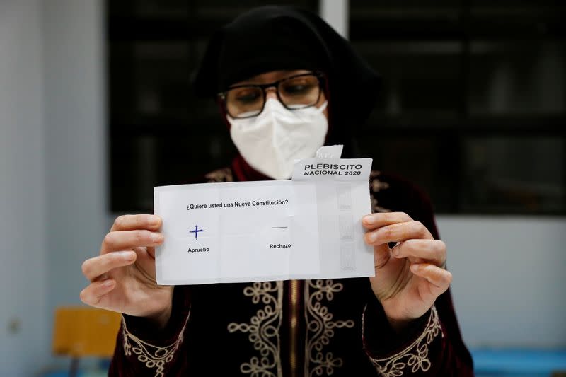 Una trabajadora electoral que lleva una máscara protectora muestra un voto durante un referéndum sobre una nueva constitución, en Valparaíso, Chile.