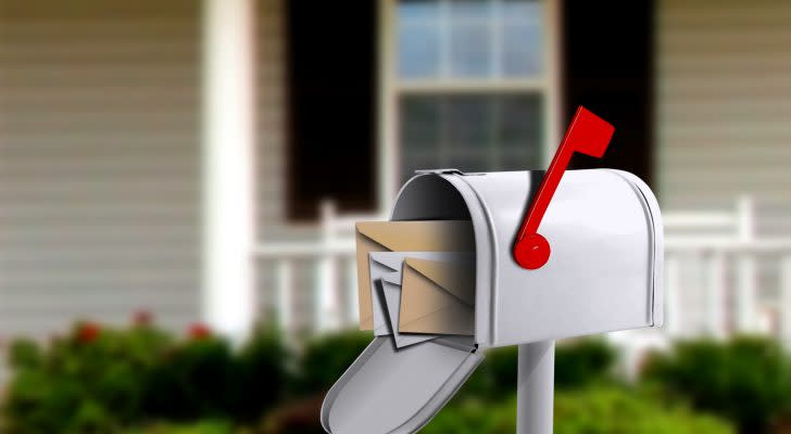 photo of a silver mailbox with red flag up and mail insider, house in background