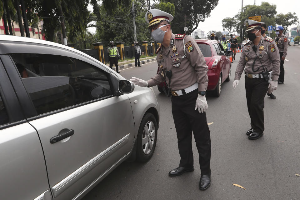 Police officers check the number of people seated inside a car during the imposition of large-scale social restriction, at a checkpoint in Jakarta, Indonesia, Friday, April 10, 2020. Authorities in Indonesia's capital kicked off a stricter restriction on Friday to slow the spread of the new coronavirus in the city where deaths from the virus has spiked in the past week. (AP Photo/Tatan Syuflana)