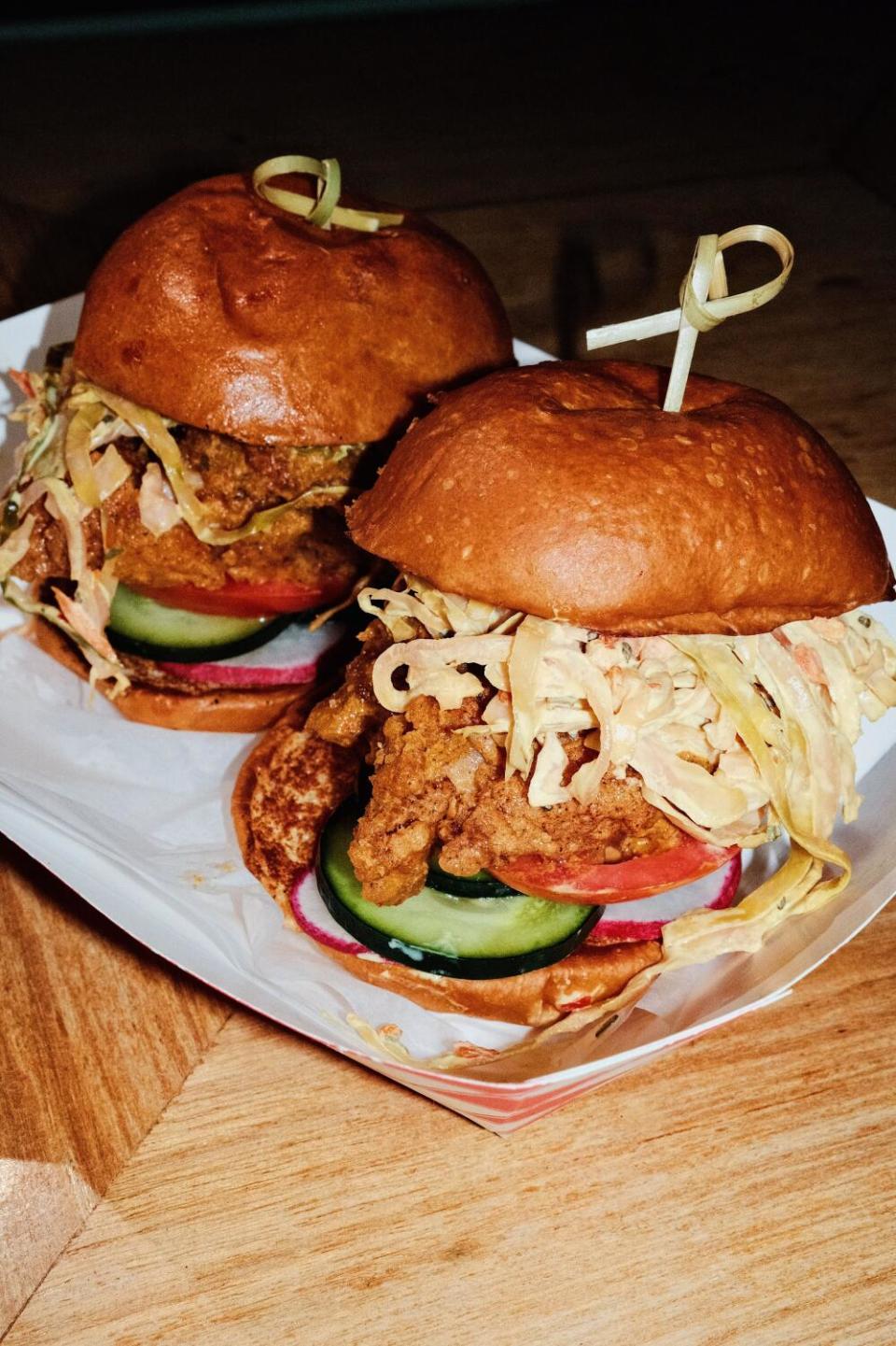 Two fried chicken sliders with slaw, cucumbers and tomato in a paper tray at Walking Spanish inside Las Perlas West Hollywood