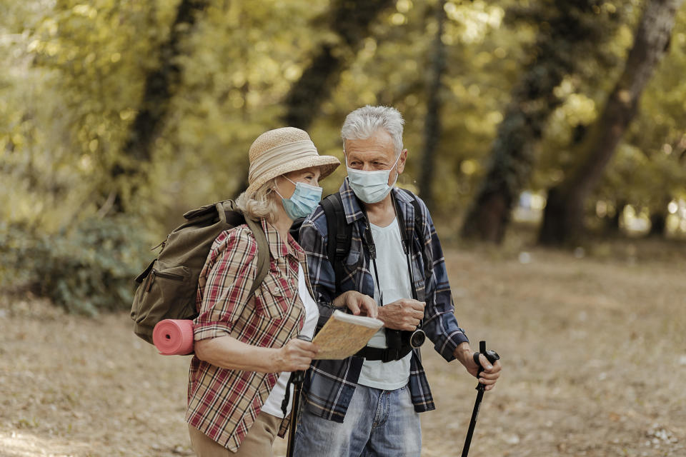 Senior Tourist Couple Travellers Hiking in Nature, Walking and Talking While Wearing Face Protective Masks During Coronavirus Outbreak. Hiking Adventure Travel People Living Active Healthy Lifestyle on COVID 19 Period