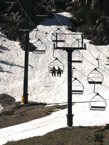 Skiers ride a chairlift over patches of snow on Mammoth Mountain.