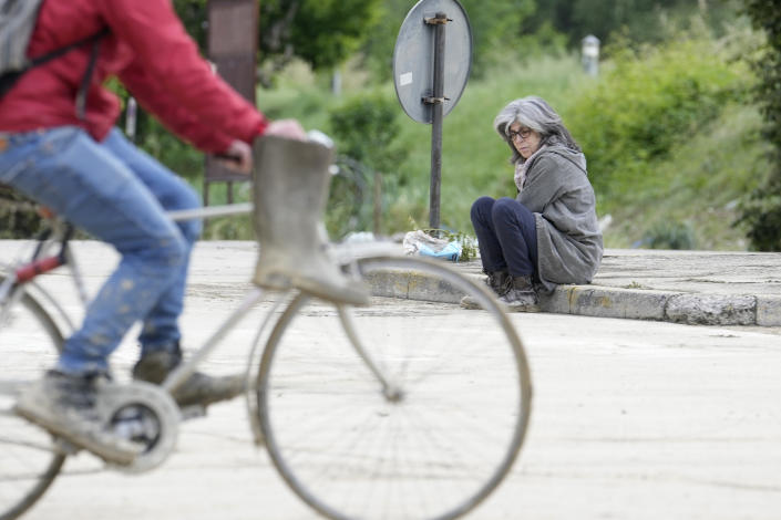 A woman sits by a road covered by mud in Faenza, Italy, Thursday, May 18, 2023. Exceptional rains Wednesday in a drought-struck region of northern Italy swelled rivers over their banks, killing at least nine people, forcing the evacuation of thousands and prompting officials to warn that Italy needs a national plan to combat climate change-induced flooding. (AP Photo/Luca Bruno)