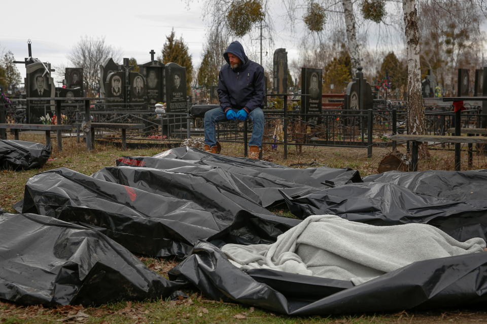 A funeral service employee sits next to bodies of civilians, collected from streets for a local cemetery at Bucha, Ukraine.