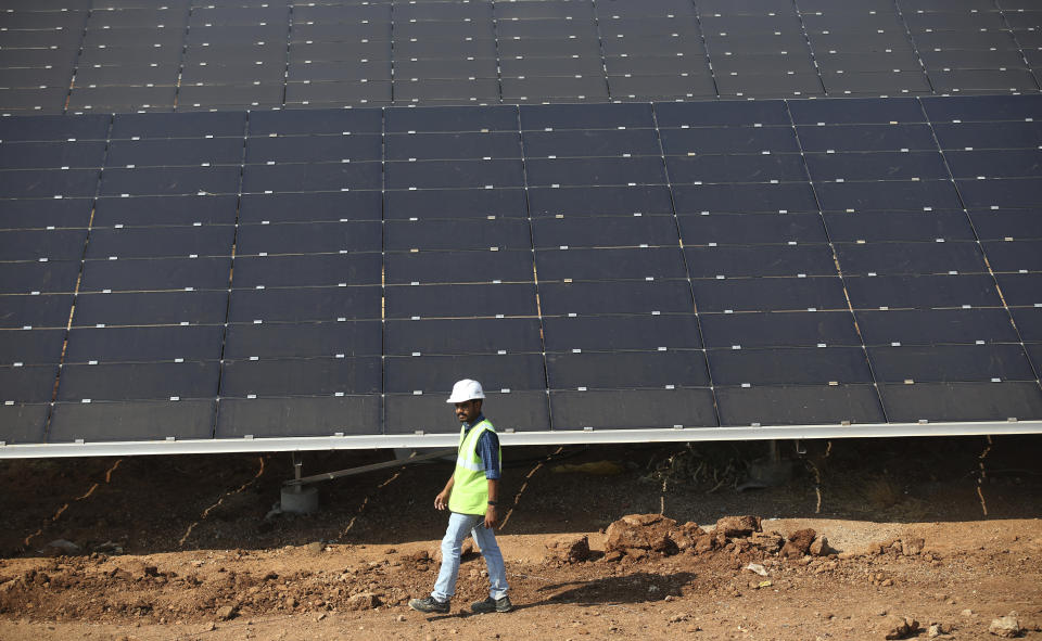 FILE - An official walks past solar panels installed at the Pavagada Solar Park north of Bangalore, India, March 1, 2018. Renewable projects have grown steadily in India for years, but a mix of policy decisions, politics and supply chain issues have slowed progress on solar projects in 2023. (AP Photo/Aijaz Rahi, File)