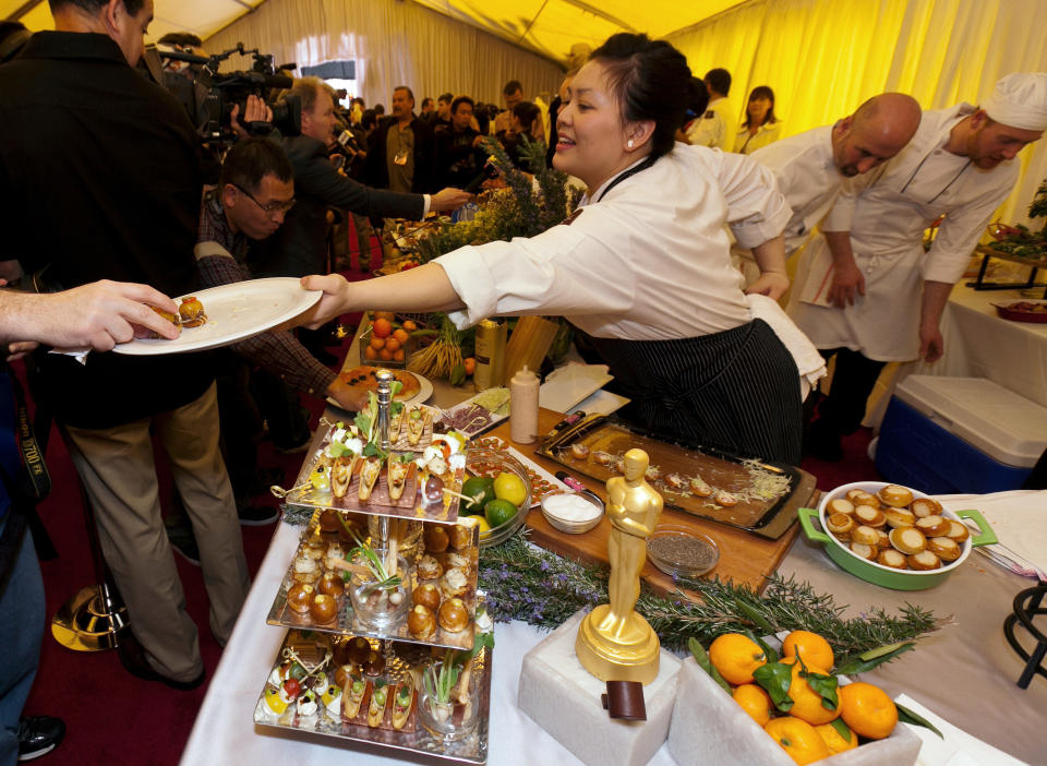 Chef Diana McDonnell, right, serves mini kobe cheeseburgers with remoulade and aged cheddar, a dish from Wolfgang Puck's planned menu at the Oscar food and beverage preview at the Kodak Theatre in Los Angeles on Thursday, Feb. 23, 2012. The dish will be served at the 84th Annual Academy Awards Governors Ball on Sunday. (AP Photo/Damian Dovarganes)