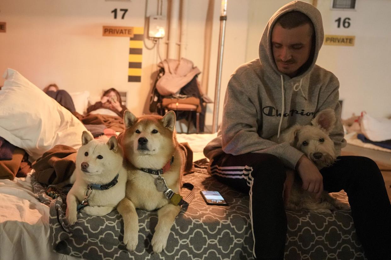 A man sits next to his dogs on mattress in a hotel underground parking turned into a bomb shelter during an air raid alert in Kyiv, Ukraine, Sunday, Feb. 27, 2022. Terrified men, women and children sought safety inside and underground, and the government maintained a 39-hour curfew to keep people off the streets as more than 150,000 Ukrainians fled to neighboring countries and the United Nations warned the number could grow to 4 million if fighting escalates.