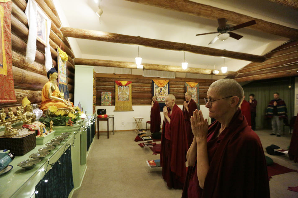 Thubten Chonyi, right, a fully ordained Buddhist nun, and other residents and guests stand in prostration during the morning meditation session at Sravasti Abbey, Thursday, Nov. 18, 2021, in Newport, Wash. (AP Photo/Young Kwak)