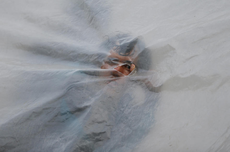 In this Nov. 13, 2018 photo, a Venezuelan migrant peeks through a hole in a tent made with plastic tarp, at a makeshift migrant settlement near the main bus terminal in Bogota, Colombia, on the day authorities opened a new, refugee-style camp for Venezuelan migrants who relocate voluntarily. Officials were initially reluctant to open camps for homeless arrivals but now say they have no choice as the number fleeing their nation's economic and humanitarian crisis continues to rapidly escalate. (AP Photo/Fernando Vergara)