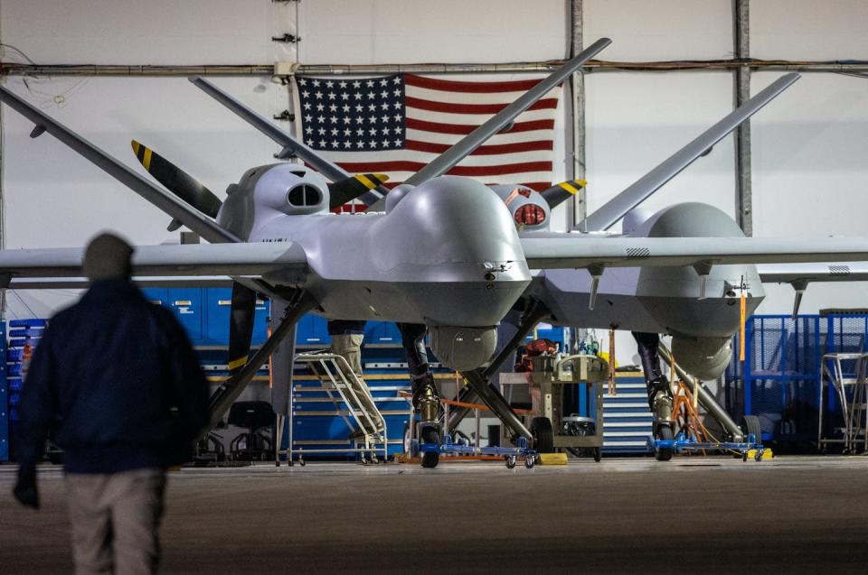 A large grey drone is stationary in front of a large American flag.