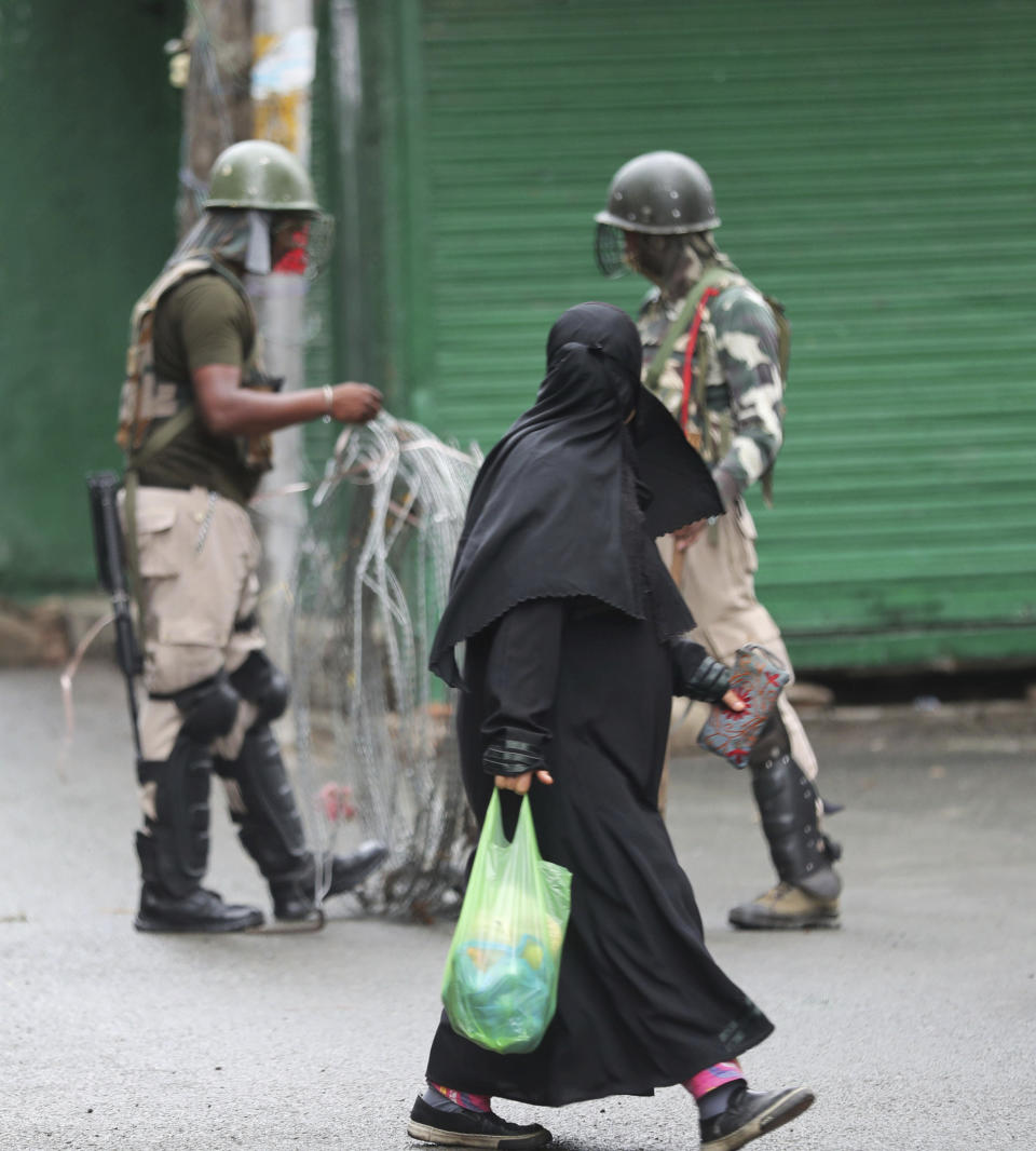 A Kashmiri woman walks past Indian paramilitary soldiers closing off a street with barbwire in Srinagar, Indian controlled Kashmir, Saturday, Aug. 10, 2019. Authorities enforcing a strict curfew in Indian-administered Kashmir will bring in trucks of essential supplies for an Islamic festival next week, as the divided Himalayan region remained in a lockdown following India's decision to strip it of its constitutional autonomy. The indefinite 24-hour curfew was briefly eased on Friday for weekly Muslim prayers in some parts of Srinagar, the region's main city, but thousands of residents are still forced to stay indoors with shops and most health clinics closed. All communications and the internet remain cut off. (AP Photo/Mukhtar Khan)