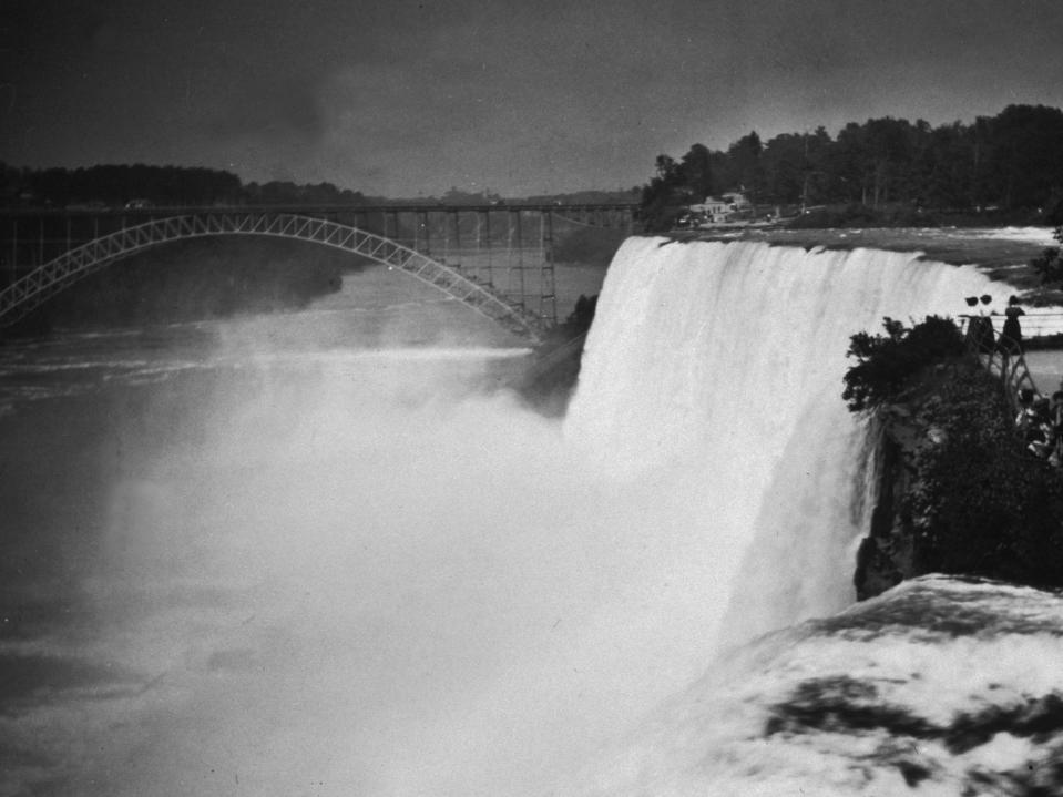 Spectators observe the American Falls and steel arch bridge from Goat Island, Niagara Falls, New York in 1895.