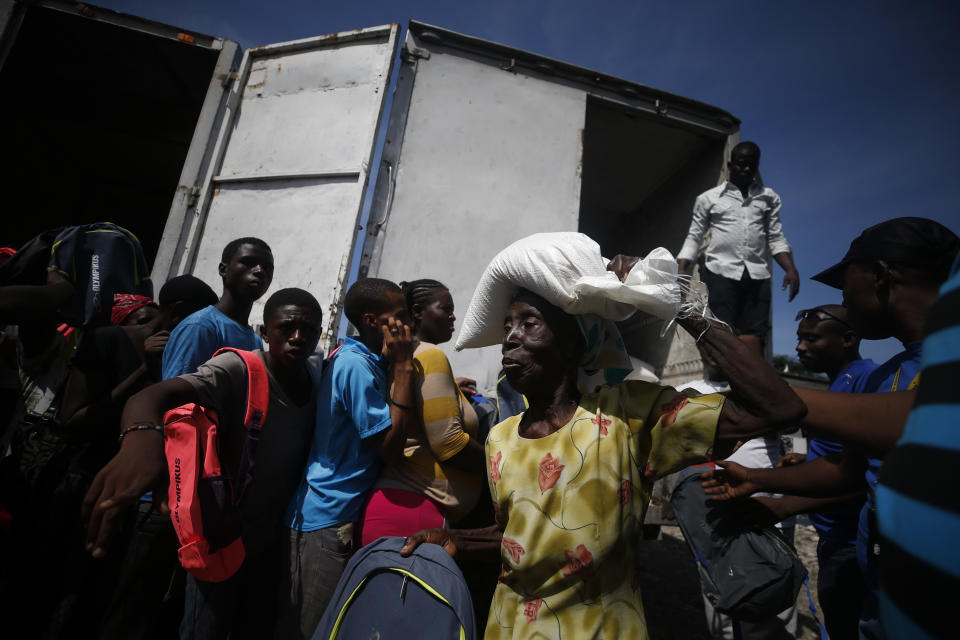 An elderly woman carries away a sack of rice during a federal government distribution of food and school supplies to some residents of Cite Soleil, in Port-au-Prince, Haiti, Thursday, Oct. 3, 2019. The daily struggles of Haitians have only become more acute as recent anti-government protests and roadblocks force the closure of businesses, sometimes permanently, as people lose jobs and dwindling incomes fall behind a spike in prices. (AP Photo/Rebecca Blackwell)