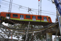 A subway car is prepared to be lowered to the ground, with the help of a crane, from a collapsed elevated section of the metro, in Mexico City, Tuesday, May 4, 2021. The elevated section of the Line 12 metro collapsed late Monday, killing at least 23 people and injuring at least 79, city officials said. (AP Photo/Marco Ugarte)