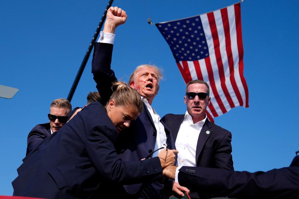 Trump, with blood on his face, raises his fist triumphantly during a rally.