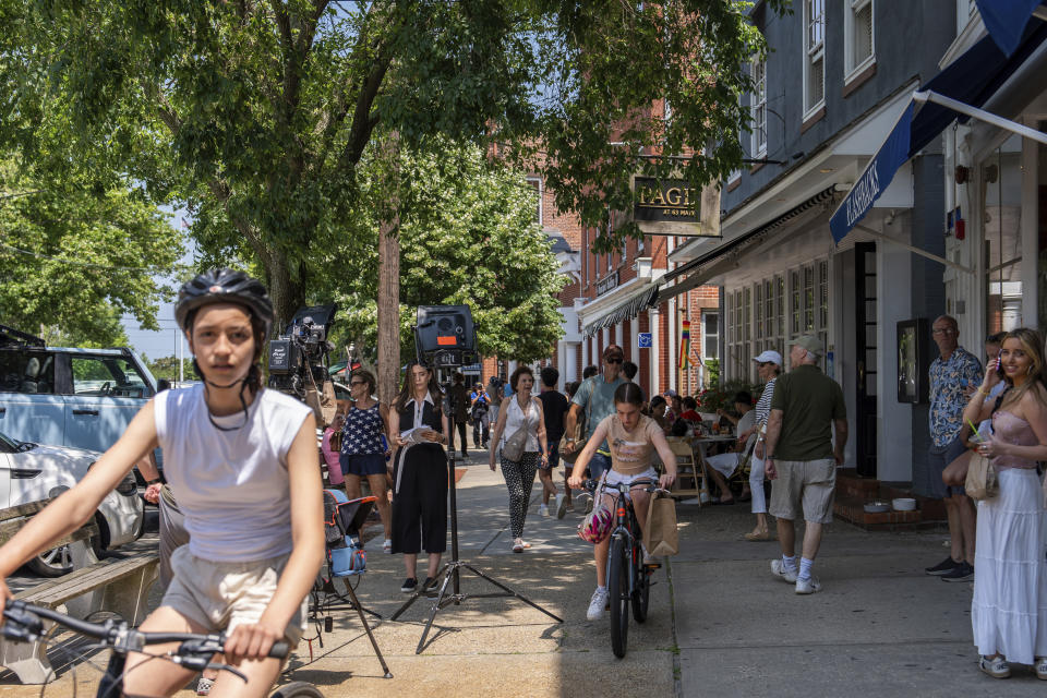 People walk and ride bikes along Main Street as a reporter does a stand up, Tuesday, June 18, 2024, in Sag Harbor, N.Y. Pop star Justin Timberlake was charged early Tuesday with driving while intoxicated in Sag Harbor after police said he ran a stop sign and veered out of his lane in the posh seaside summer retreat. (AP Photo/Julia Nikhinson)