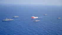 In this photo provided by the Turkish Defense Ministry, Turkey's research vessel, Oruc Reis, in red and white, is surrounded by Turkish navy vessels as it was heading in the west of Antalya on the Mediterranean, Turkey, Monday, Aug 10, 2020. Tension remains high between Greece and Turkey, whose warships are in the eastern Mediterranean where Turkey has sent a research vessel to carry out seismic research for energy resources in an area Greece says is on its continental shelf.(Turkish Defense Ministry via AP, Pool)