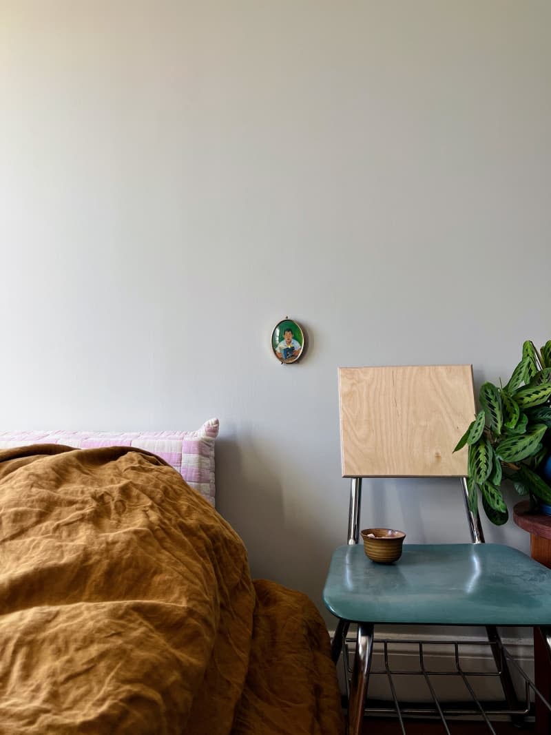 Bedroom with brown linen comforter with a vintage school desk chair as a nightstand and a small oval painting hanging on the wall