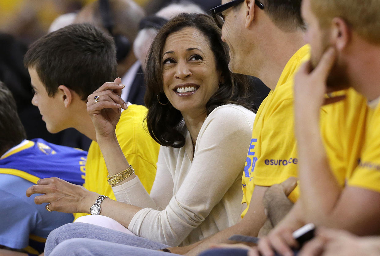 Kamala Harris shown surrounded by fans in yellow shirts at a basketball game. 