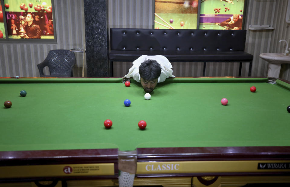 Mohammad Ikram plays snooker with his chin at a local snooker club in Samundri town, Pakistan, Sunday, Oct. 25, 2020. Ikram, 32, was born without arms, but everyone simply admires his snooker skills when he hits the cue ball with his chin and pots a colored ball on a snooker table. He lives in a remote rural town of Punjab province and his physical disability doesn't come in his way to fulfill his childhood dream of playing the game of snooker. (AP Photo/Anjum Naveed)