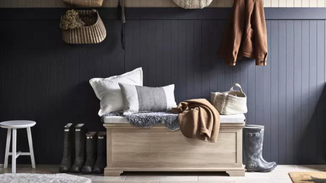  A dark blue entryway with a storage ottoman and hanging coats 