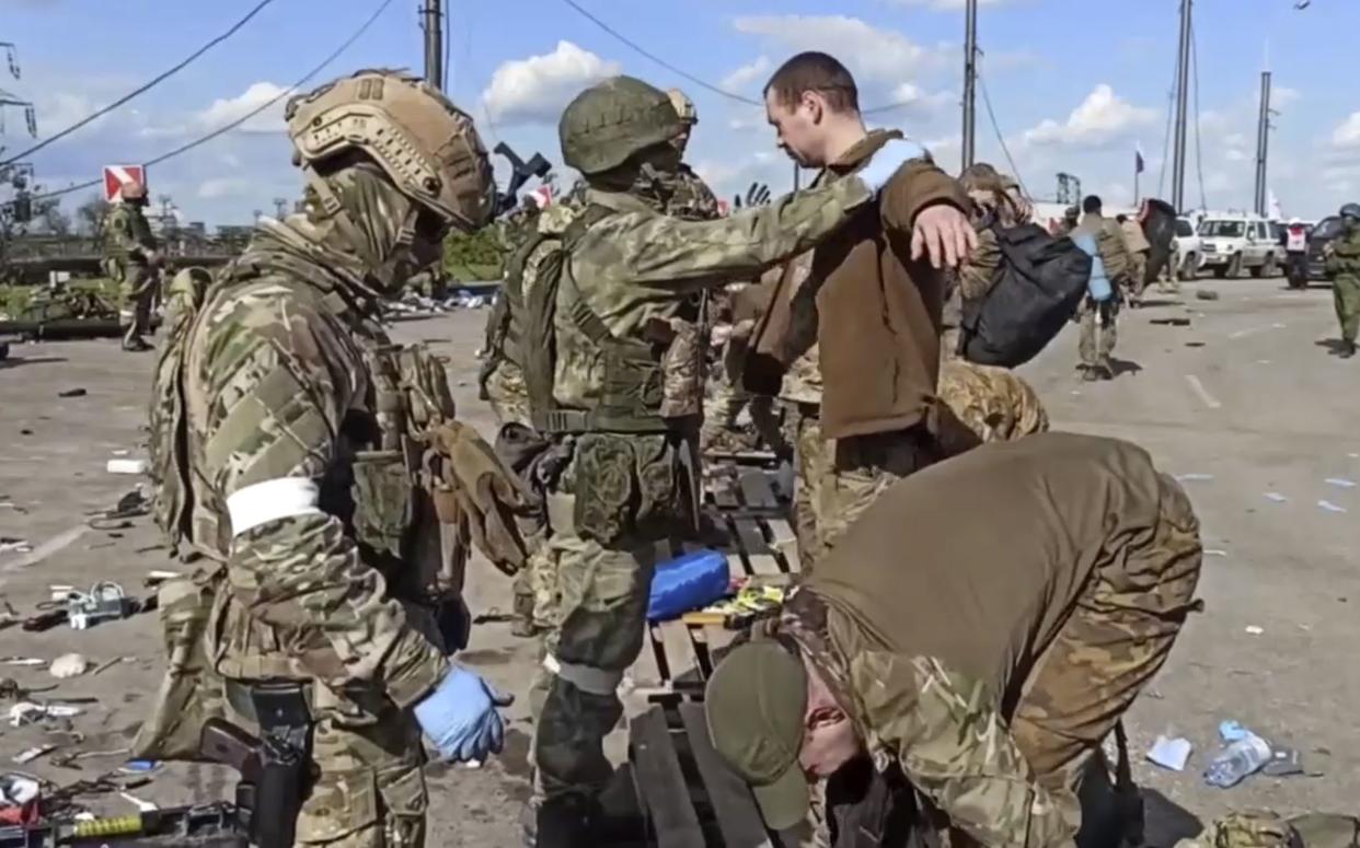 In this photo taken from video released by the Russian Defense Ministry on Friday, May 20, 2022, Russian servicemen frisk Ukrainian servicemen after they leaved the besieged Azovstal steel plant in Mariupol. (Russian Defense Ministry Press Service via AP)