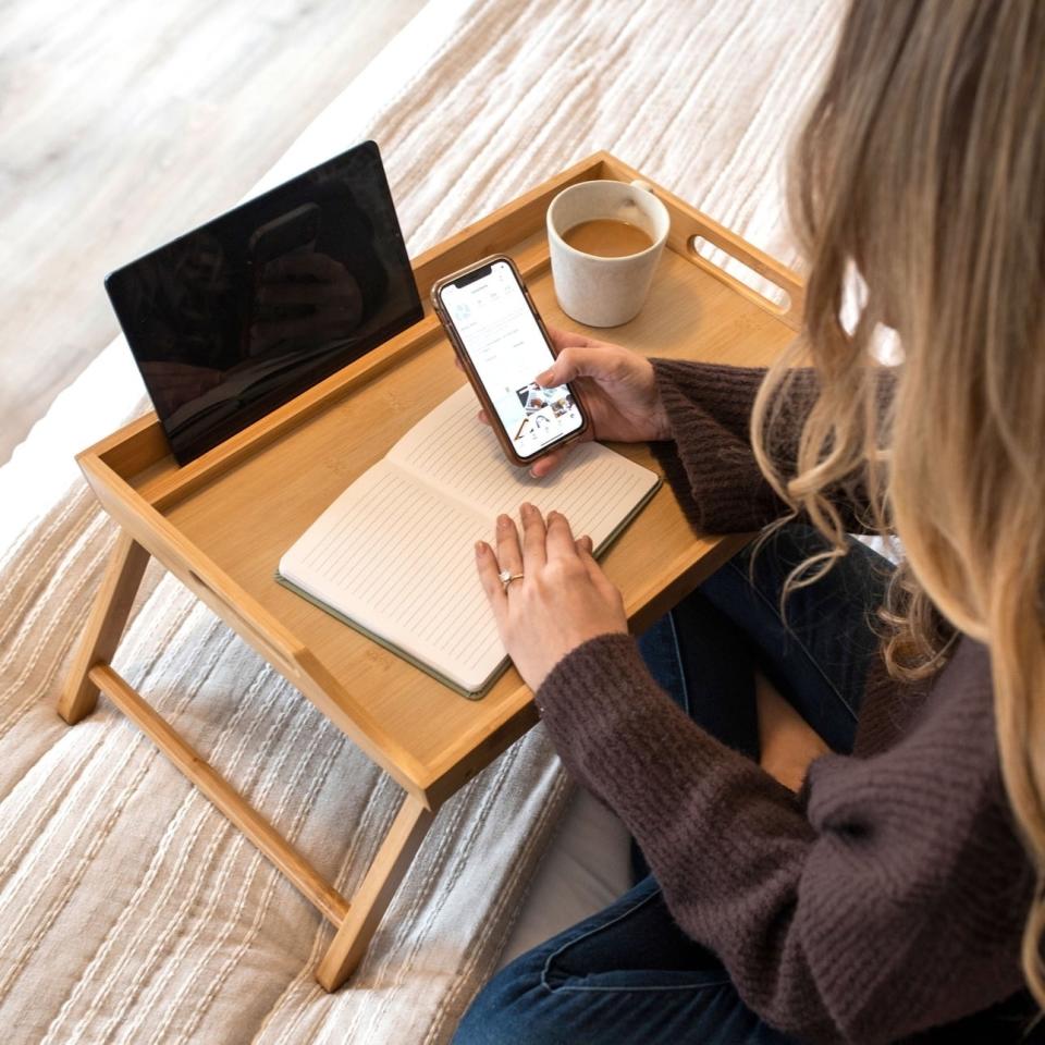 Model uses beige tray table with journal and tablet while sitting on bed