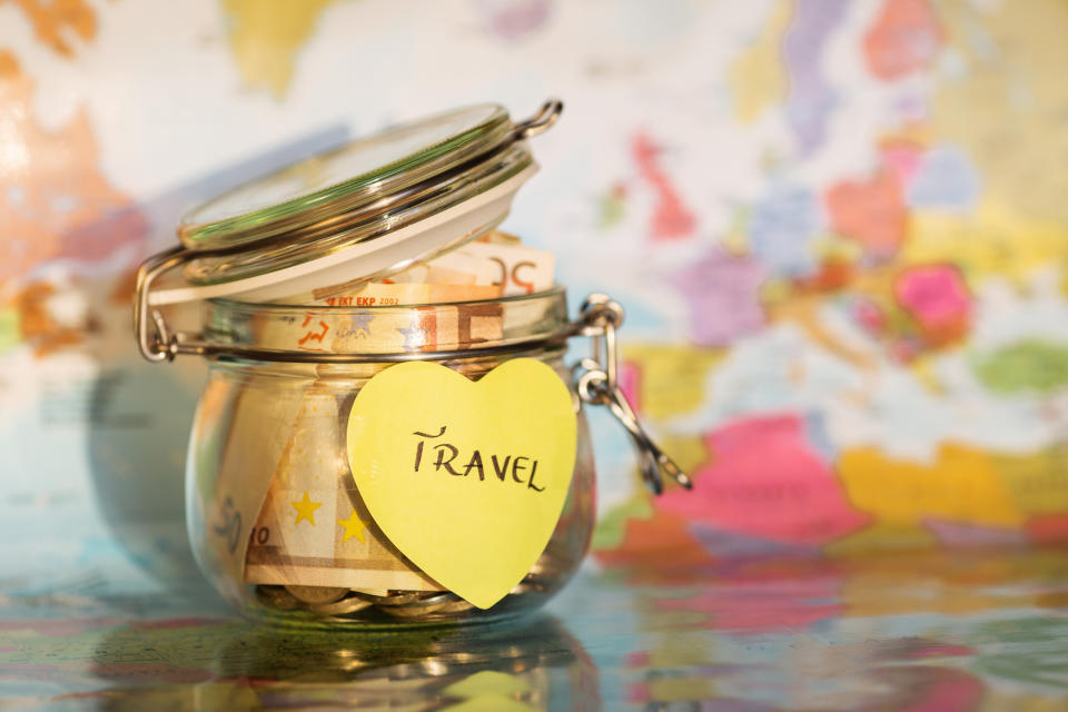 Glass jar with money on a map marked with a 'Travel' sticker, symbolizing saving for trips