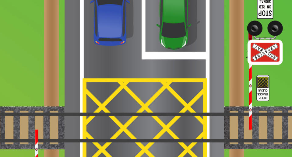 A green car is pictured waiting at a railway crossing.