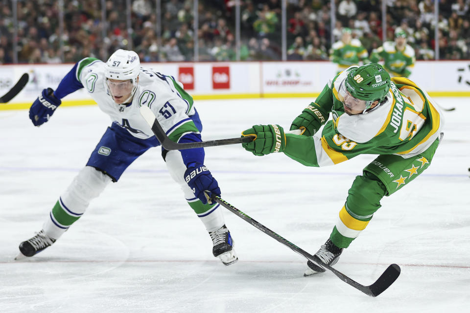 Minnesota Wild left wing Marcus Johansson, right, shoots along side Vancouver Canucks defenseman Tyler Myers (57) during the second period of an NHL hockey game Saturday, Dec. 16, 2023, in St Paul, Minn. (AP Photo/Matt Krohn)