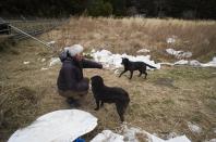 Naoto Matsumura pets his dogs during an interview with The Associated Press at his farm land in Tomioka town, Fukushima prefecture, northeastern Japan, Friday, Feb. 26, 2021. About 10 kilometers (6 miles) south of the wrecked Fukushima Dai-ichi nuclear power plant, rice farmer Matsumura defied a government evacuation order and stayed on his farm to protect his land the cattle abandoned by neighbors a decade ago. (AP Photo/Hiro Komae)