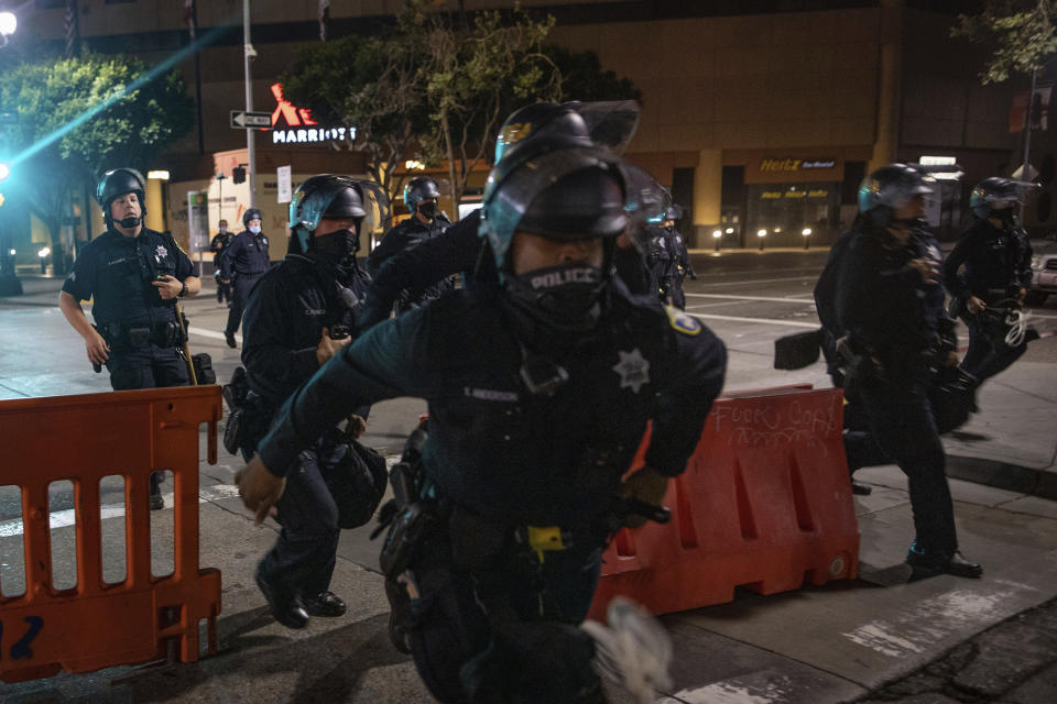 Police chase after protesters who refused to disperse at a protest on Saturday, July 25, 2020, in Oakland, Calif. Protesters in California set fire to a courthouse, damaged a police station and assaulted officers after a peaceful demonstration intensified late Saturday, Oakland police said. (AP Photo/Christian Monterrosa)